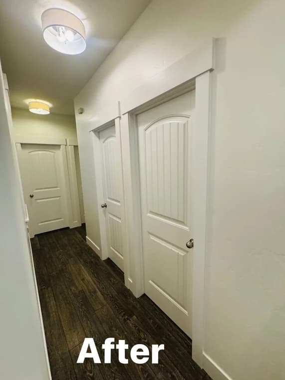 This is an image from Montenegro's Painting & Construction LLC company, located in Meridian, ID The image is an interior hallway makeover with freshly painted white paneled doors, clean white trim, and dark wood-look flooring, completed by Montenegro's Painting & Construction, LLC