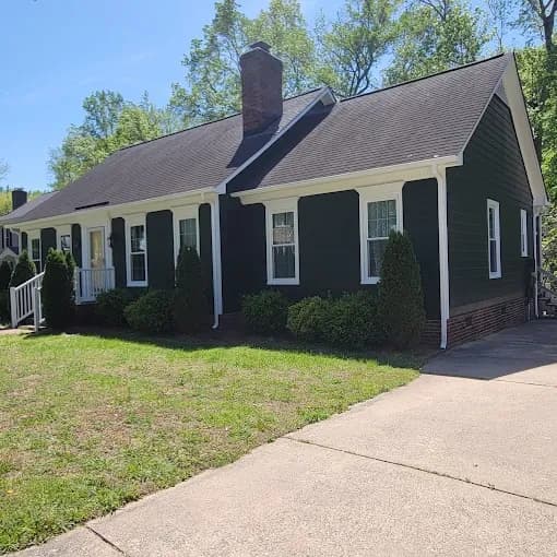 Exterior painting project by That 1 Painter Charlotte - Fort Mill in Charlotte, NC. The image shows a black single-story home with white trim and a brick chimney.