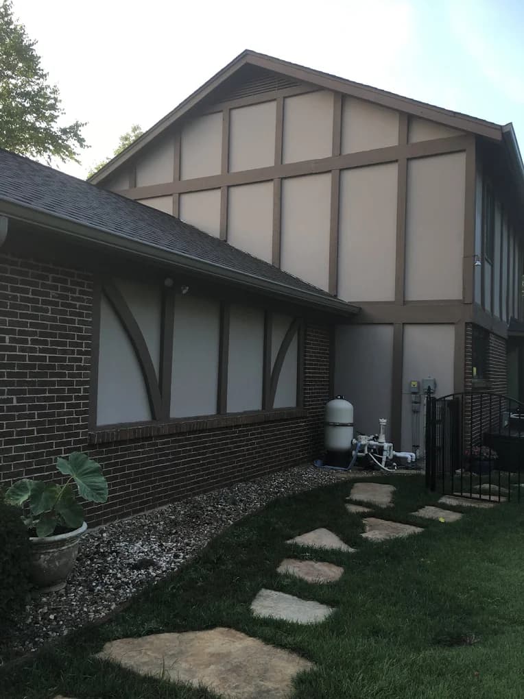 Exterior painting project by Color Concepts Painting Inc. in Alton, Illinois. The image shows a Tudor-style home with beige stucco, brown trim, brick walls, and a walkway.