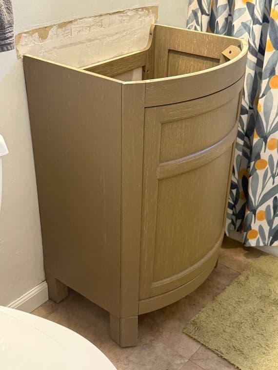 Light brown wooden bathroom vanity cabinet with a curved door, installed against a wall.