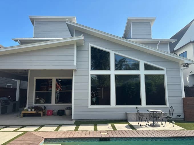"This is an image from Squared Away Painting, located in Texas. The photo shows a freshly painted modern home exterior with light gray siding, large geometric windows, and a clean outdoor living area beside a pool."