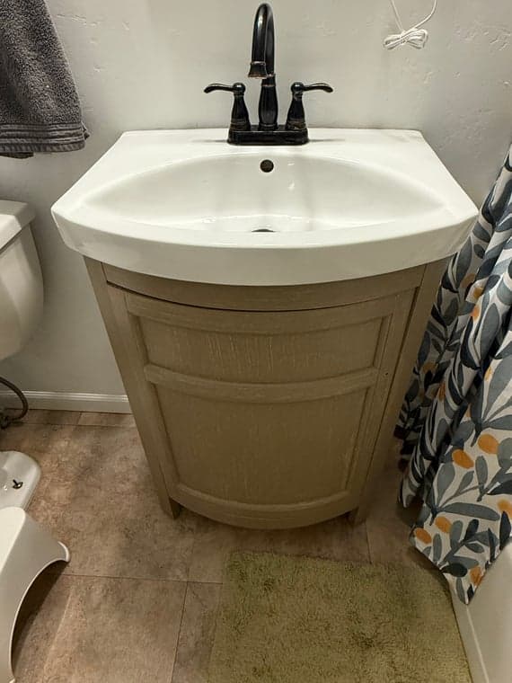 Installed light gray bathroom vanity with a white ceramic sink and modern black faucet.