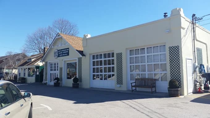 This is an image from Chameleon Painting Inc., located in New York. The photo shows a light yellow commercial building with large white garage-style doors, decorative lattice panels, and a bench placed outside near the entrance.