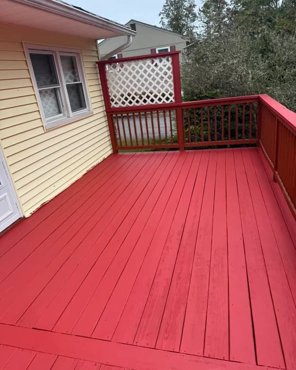 This is an image from Jay's Pro Painting, located in New York. The image shows a bright red freshly painted wooden deck with matching railings next to a yellow-sided house.