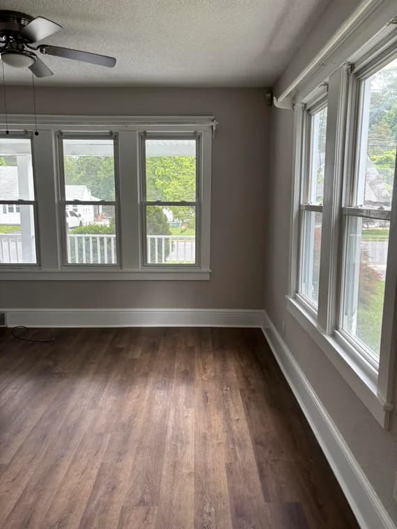 An interior room with large windows and natural light, painted in soft gray with crisp white trim by WallPro Painting & Design, paired with dark wood floors.