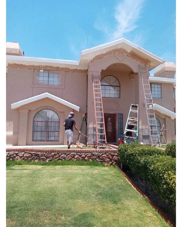 "This is an image from El Paso Paint Kings, located in Texas. The photo shows painters working on the exterior of a large two-story home with ladders set up as they prepare and paint the front façade."