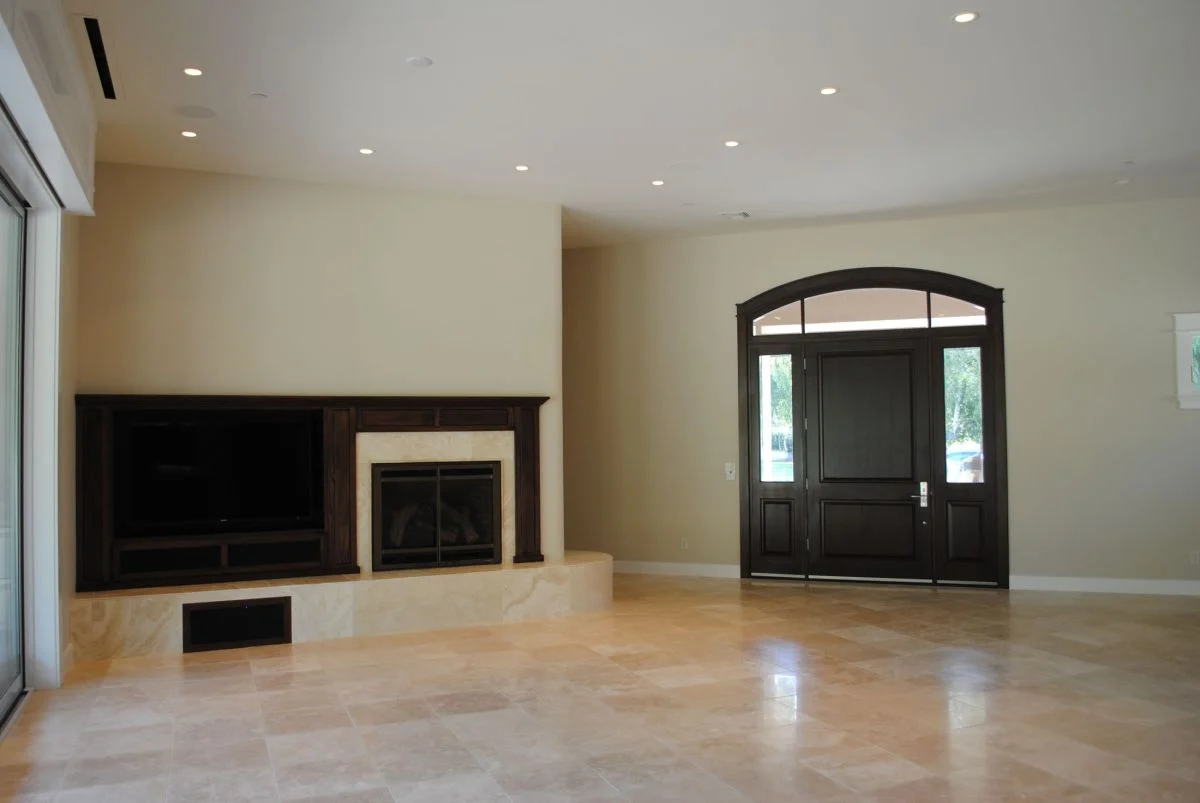 This is an image from Brooks Painting, located in California. The image is from Brooks Painting and shows interior painting in a spacious living room with a dark wood front door, recessed lighting, and a built-in fireplace surround.