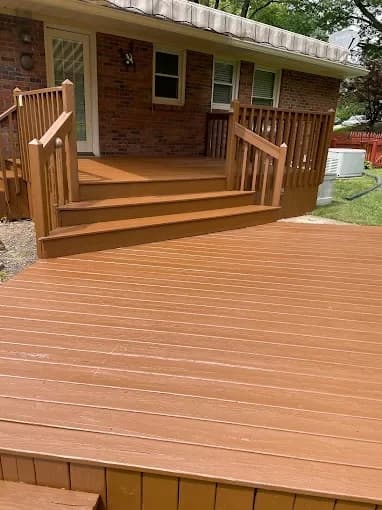 This is an image from R.E.A.L. Painting, located in Kentucky. The photo shows a freshly painted wooden deck and stairs in a rich brown finish attached to a brick house.