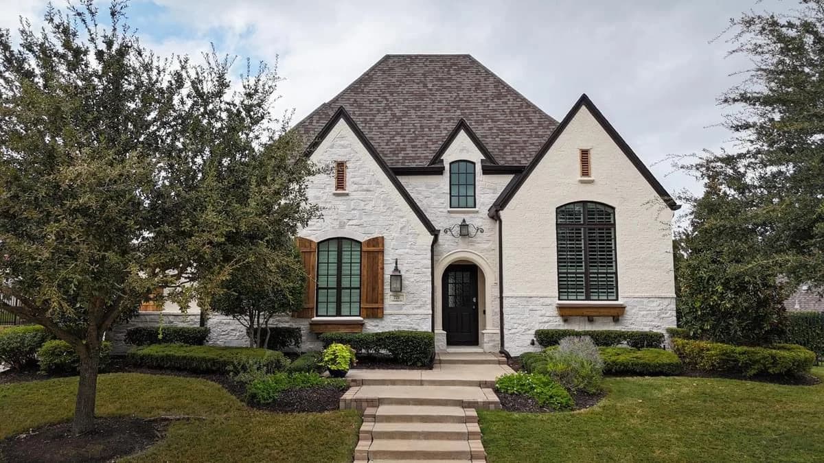 "This is an image from Highland Painting Co., located in Texas. The photo shows a white painted brick home with dark trim, wooden shutters, and tidy landscaping across the front lawn."