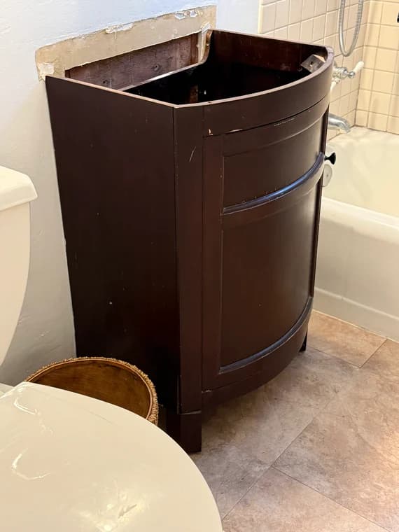 Old dark brown bathroom vanity base awaiting replacement during bathroom renovation