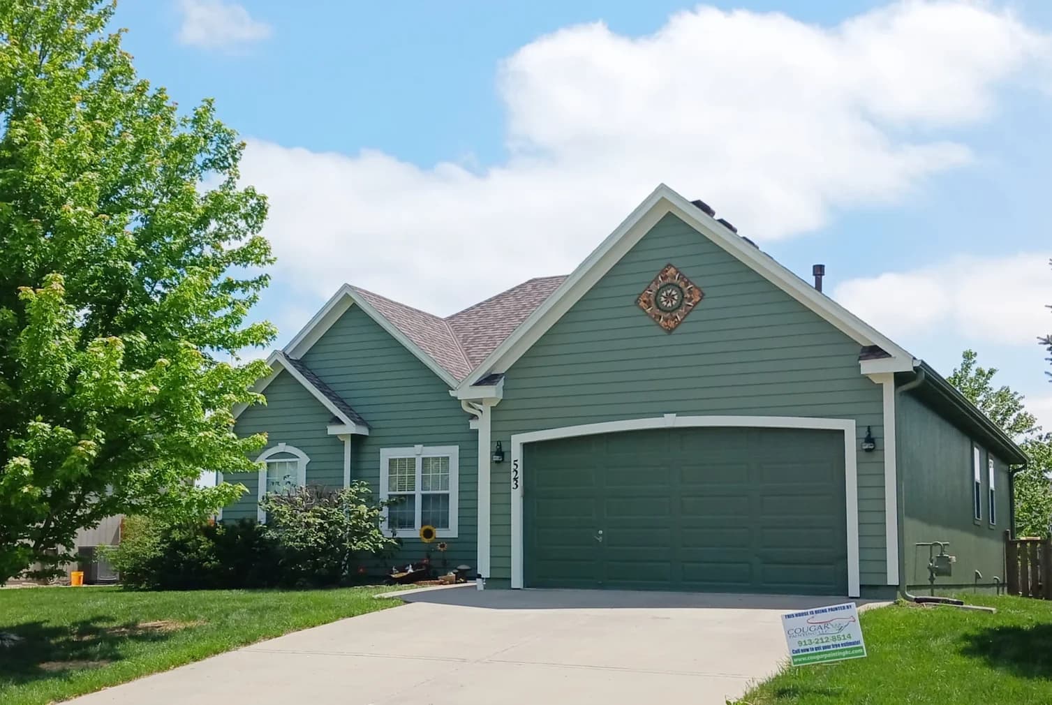 This is an image from Cougar Painting LLC. The image is of an exterior house in Kansas City KS with freshly painted green siding, white trim, and a two-car garage.