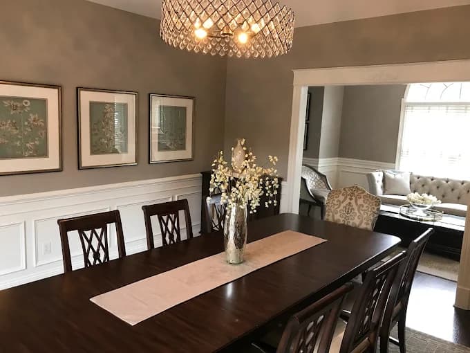 This is an image from Paul’s Painting & Powerwashing, located in New Jersey. The image shows a formal dining room with freshly painted walls, decorative wainscoting, framed wall art, and a chandelier above a dark wood table.
