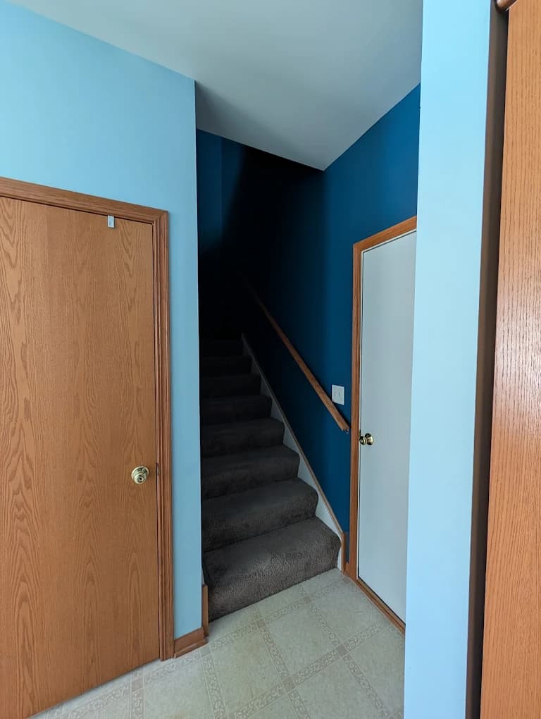 Interior painting project by Allegiant Painting LLC in Lakemoor, Illinois. The image shows light blue walls, a dark blue stairwell, wood trim, and carpeted stairs.