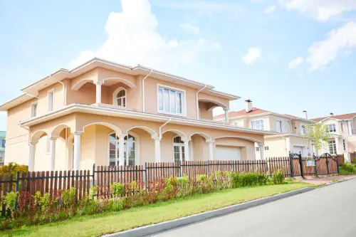 This is an image from The Woodlands Paint Doctor, located in Texas. The picture shows a beige two-story house with arched exterior details, a fenced yard, and a neatly maintained front landscape.