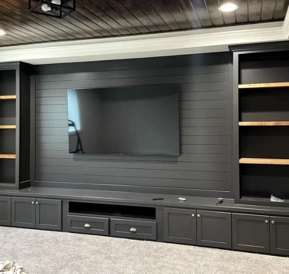 This is an image from Stone Painting. The image shows a dark built-in entertainment wall with shelving, a mounted TV, and wood accents in a finished living space.