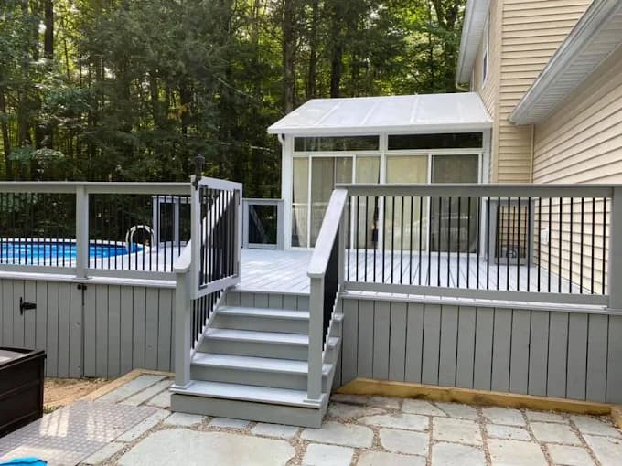 This is an image from JT’s Painting 518 LLC, located in New York. The image shows a newly painted outdoor deck with gray railings, white steps, and a clean, uniform finish surrounding a backyard pool area.