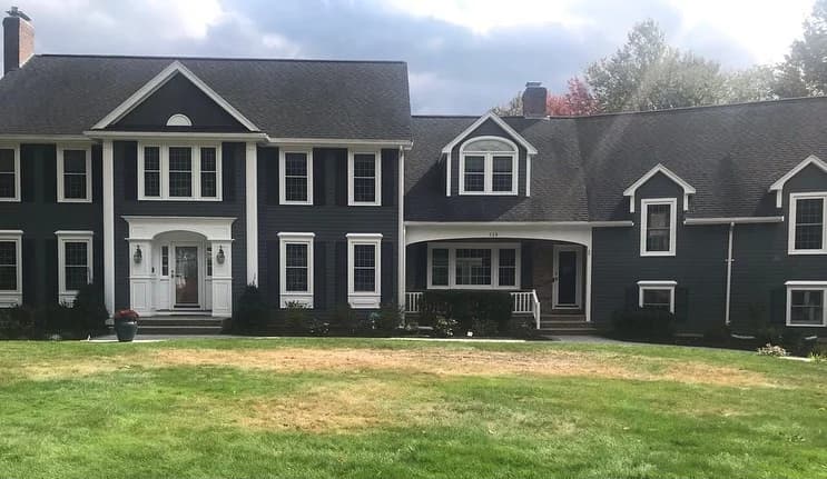 This is an image from Ulta Home, located in Massachusetts. It shows a large dark gray house with white trim and a well-maintained front yard, demonstrating the company’s exterior painting expertise.