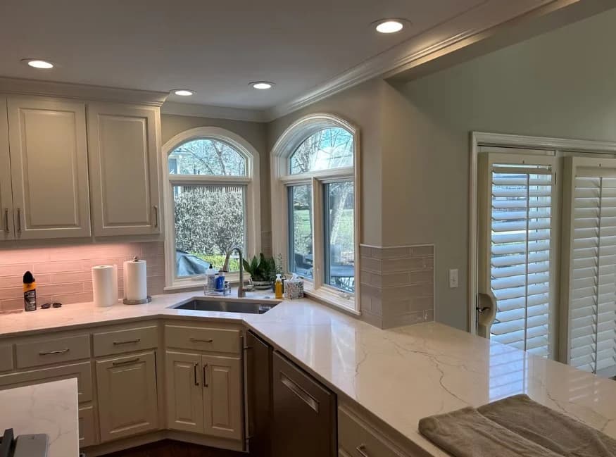 This is an image from Odyssey Painting. The image shows a bright kitchen with cream cabinetry, marble countertops, arched windows, and recessed lighting.