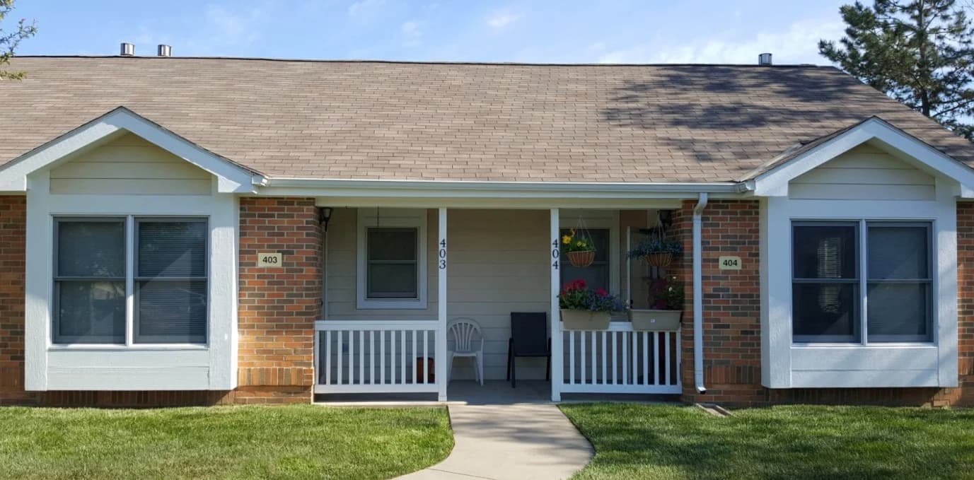 This is an image from West & Co Painting, LLC. The image shows a duplex with tan siding, white trim, brick accents, and a shared front porch with flowers and chairs.