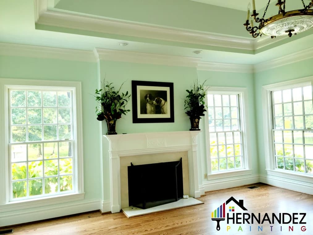 This is an image from Hernandez Painting, located in Tennessee. The interior photo showcases a bright living room with mint green walls, white trim, and a decorative fireplace between large windows.