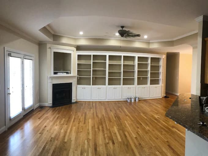 Interior painting project by Roca's Painters LLC in Mebane, North Carolina. The image shows white built-in shelves, a fireplace, and hardwood floors.