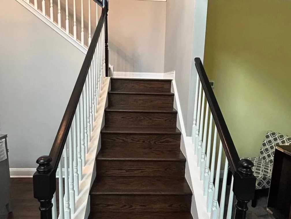 This is an image from MK Painting & Custom Finishes Co company, located in Schwenksville, PA. The image is a MK Painting project featuring dark wood stair treads with white spindles and black railings in residential entrywa