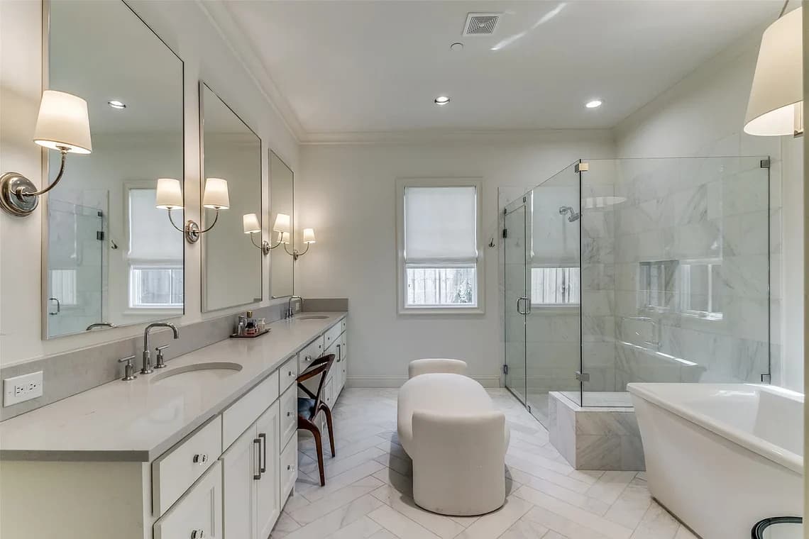 "This is an image from Highland Painting Co., located in Texas. The bathroom features white cabinetry, a long double vanity, a glass-enclosed shower, and a freestanding bathtub with marble-style tile throughout."