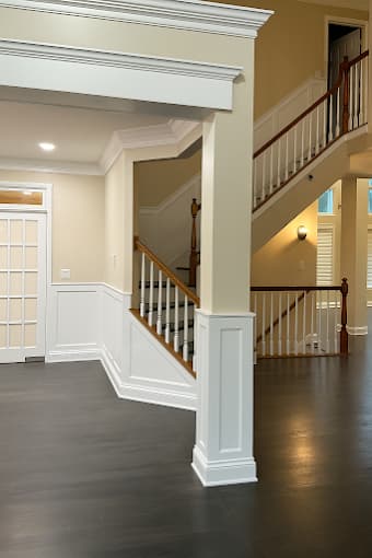 Interior painting project by Metanoia Construction Inc. in Elburn, Illinois. The image shows a white foyer with paneled walls, columns, stair railings, and dark flooring.