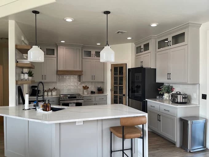 This is an image from Fixable Painting, located in Oklahoma. The photo shows a bright modern kitchen with light gray cabinetry, a large white island countertop, pendant lighting, and stainless steel appliances.