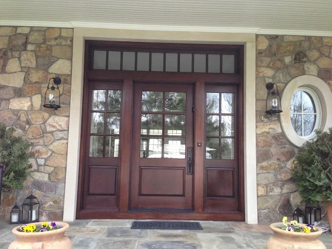This is an image from Firefly Painting Inc, located in Colorado. The entryway features a dark stained wood front door with glass panels, stone siding, and decorative lanterns on each side.