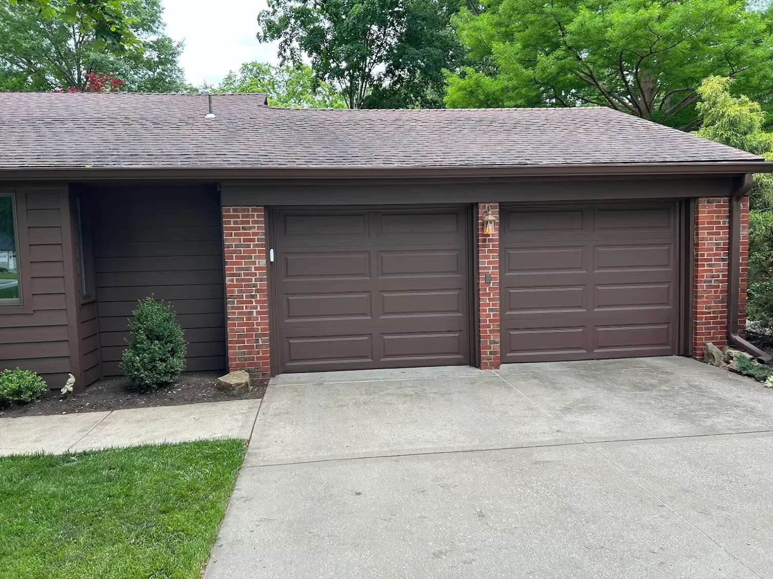 This is an image from Greg Baker Painting. The image is exterior painting in Kansas City KS showing a brown ranch-style home with matching brown garage doors and brick accents.