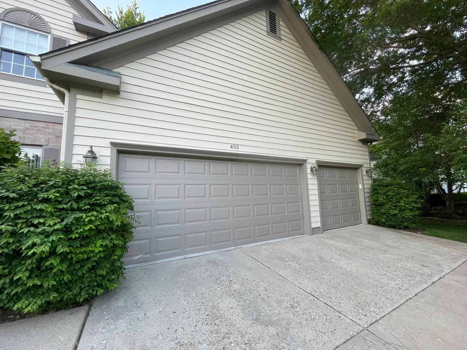 This is an image from A Plus Decorating Inc., located in Illinois. The image shows a residential home exterior with light siding, gray painted garage doors, gray trim, and a concrete driveway.