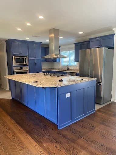 This is an image from Fresh Coat Painters of Oklahoma City, located in Oklahoma. The photo shows a modern kitchen with freshly painted deep blue cabinets, a large granite island, stainless steel appliances, and hardwood flooring.