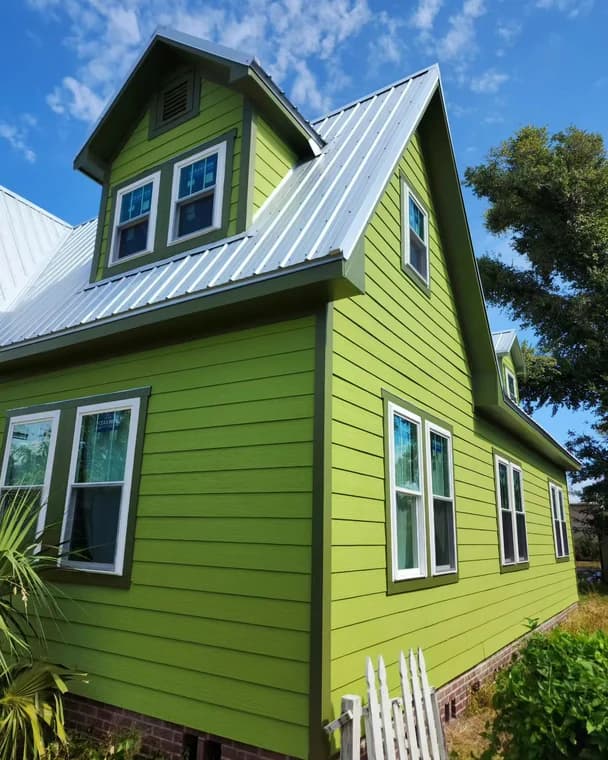 This is an image from Frank Fast Painter company, located in Panama City Beach, FL. The image is a bright green two-story house with metal roof and white trim under clear blue sky