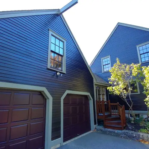 This is an image from Promark Painting, located in Massachusetts. It highlights a modern home with sleek dark siding and contrasting light trim, complemented by matching dark garage doors.