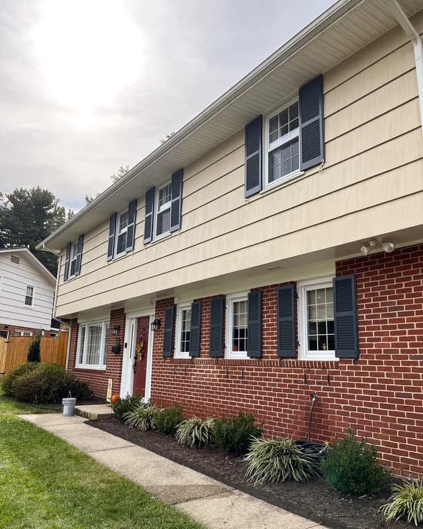 This is an image from Aurora Painting, located in Pennsylvania. The exterior photo shows a two-story home with cream siding, red brick on the lower level, and dark blue shutters along the windows.
