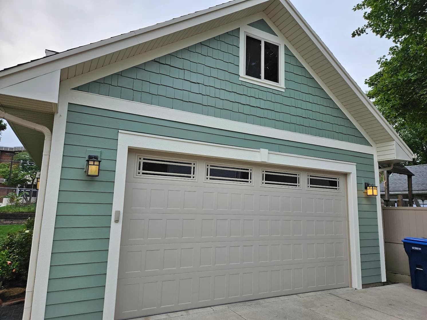 This is an image from Spray-Net Chicago West, located in Illinois. The image shows an exterior garage with teal painted siding, white trim, shake-style gable siding, and a light gray garage door.