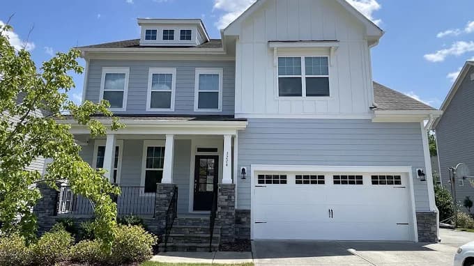 Exterior painting project by Triangle Pro Painting in Raleigh, NC. The image shows a gray two-story home with white trim, stone accents, and a garage.
