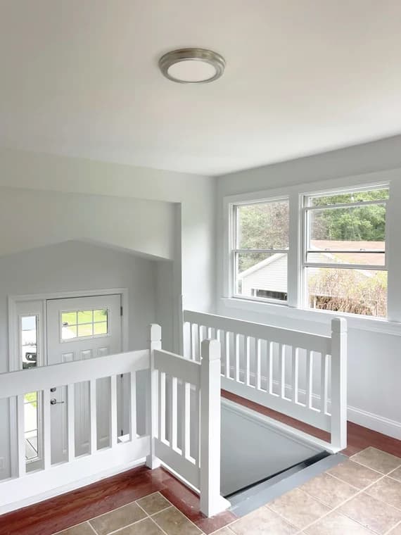 This is an image from CertaPro Painters of Orange County NY, located in New York. The photo shows a freshly painted interior stair landing with white railings, light gray walls, large windows, and a view of the front entryway below.