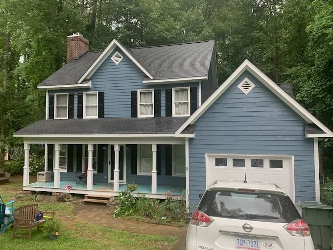 Exterior painting project by NC Paint & PowerWash in Garner, North Carolina. The image shows a blue two-story home with white trim, black shutters, and a garage.
