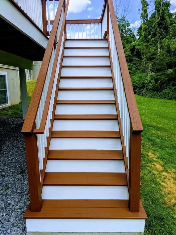 This is an image from Certified Painting, located in New York. The image shows freshly refinished exterior stairs with white risers, rich brown treads, and matching brown railings leading down to a grassy yard.