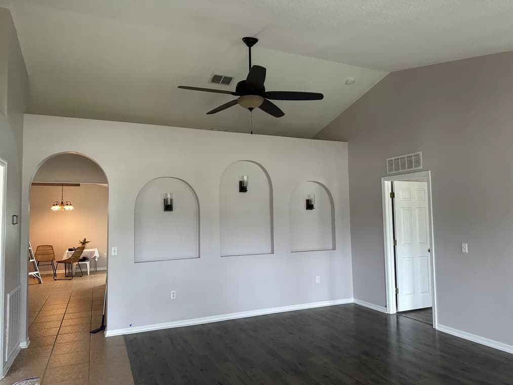 This is an image from HH Painting company, located in Gainesville, FL. The image is a freshly painted living room with vaulted ceiling, recessed wall niches, dark vinyl flooring, and neutral wall tones
