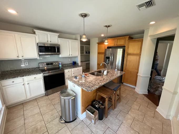 This is an image from Spell Painting, located in Louisiana. The photo shows a modern kitchen with newly painted white upper cabinets, natural wood lower cabinets, granite countertops, and stainless steel appliances for a bright, updated look.