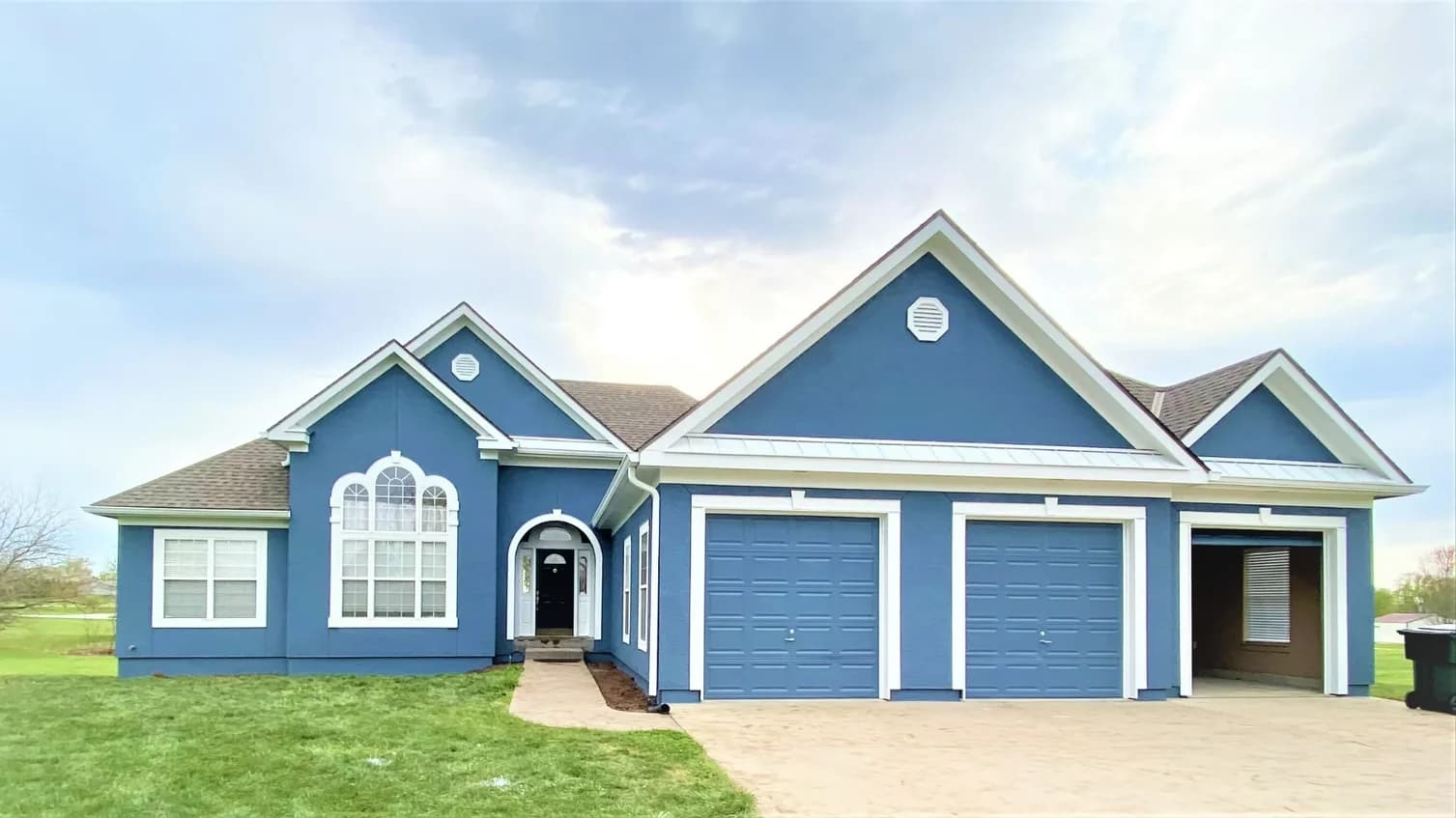 This is an image from Cougar Painting LLC. The image is of an exterior house in Kansas City KS with freshly painted blue stucco, white trim, and dual garage doors.