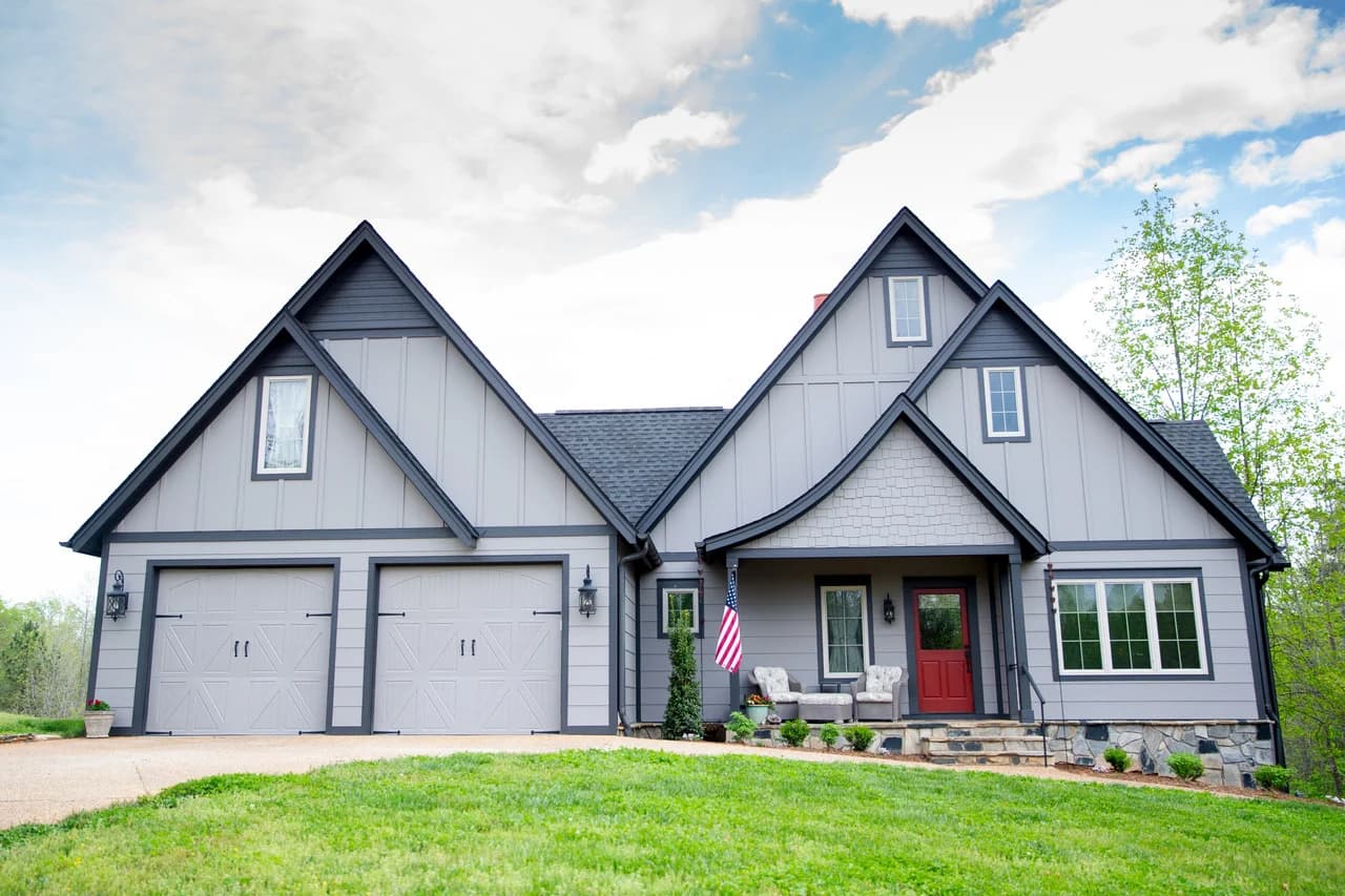 Exterior painting project by Burlett Painting, LLC in Hendersonville, North Carolina. The image shows a gray farmhouse exterior, dark trim, and a red front door.