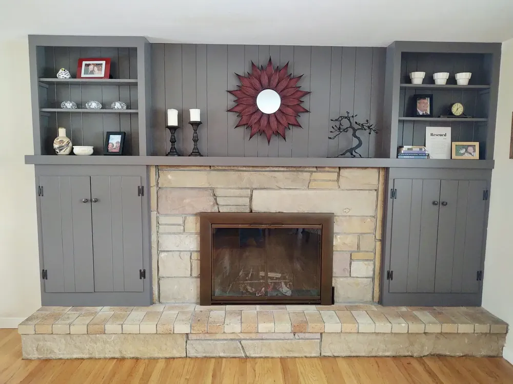 This is an image from Empire Painting Services LLC, located in New Jersey. The image shows a painted fireplace feature wall with custom built-in cabinets finished in gray, paired with a stone fireplace surround.