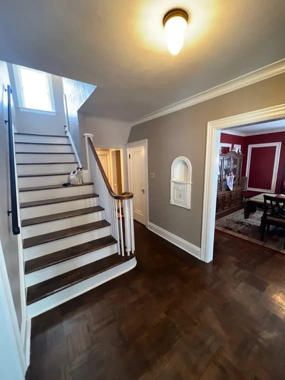 This is an image from Empire Painting Services LLC, located in New Jersey. The image shows an interior stairway and entry hallway with freshly painted neutral gray walls, white trim, and refinished hardwood floors.