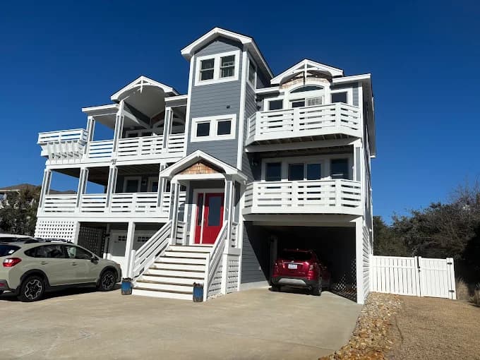 Exterior painting project by Kitty Hawk Painting in Kitty Hawk, NC. The image shows a gray coastal home with white trim, balconies, and a red door.