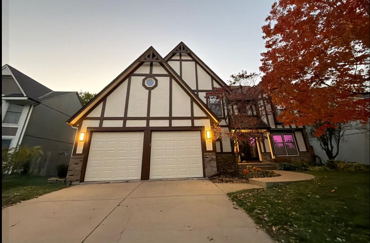 This is an image from Painter's Painting. The image is a Two-story Tudor-style home in Kansas with fresh exterior paint, double garage doors, and evening lighting.
