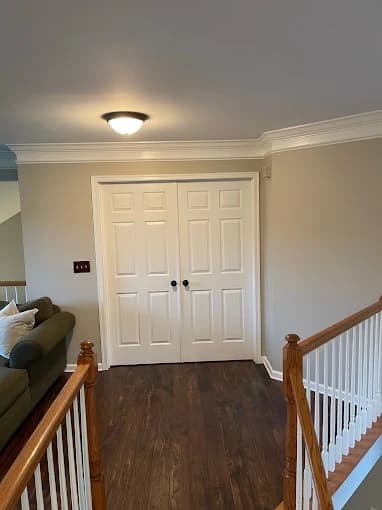 This is an image from Jay's Pro Painting, located in New York. The image shows a hallway landing with beige walls, bright white double doors, crown molding, and dark hardwood flooring.